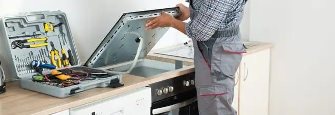 Cooktop repair technician lifting a built-in stovetop for service in Detroit, MI