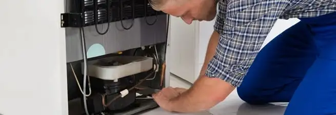 Refrigerator repair technician servicing the compressor and condenser area in Detroit, MI