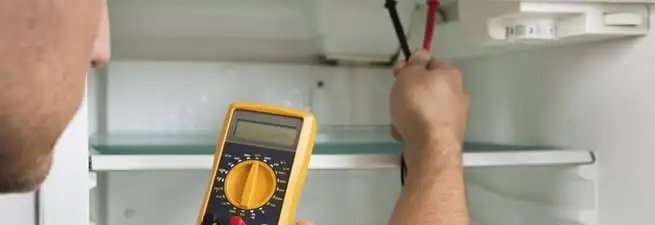 Refrigerator repair technician testing electrical components with a multimeter in Detroit, MI